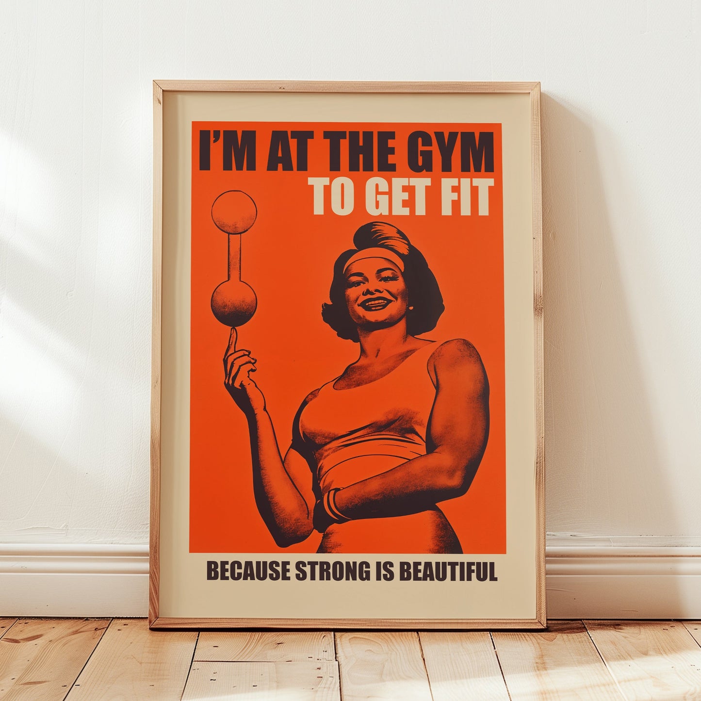 Vintage-style gym poster on an orange background featuring a muscular woman balancing a barbell on one finger with the text "I'M AT THE GYM TO GET FIT BECAUSE STRONG IS BEAUTIFUL."