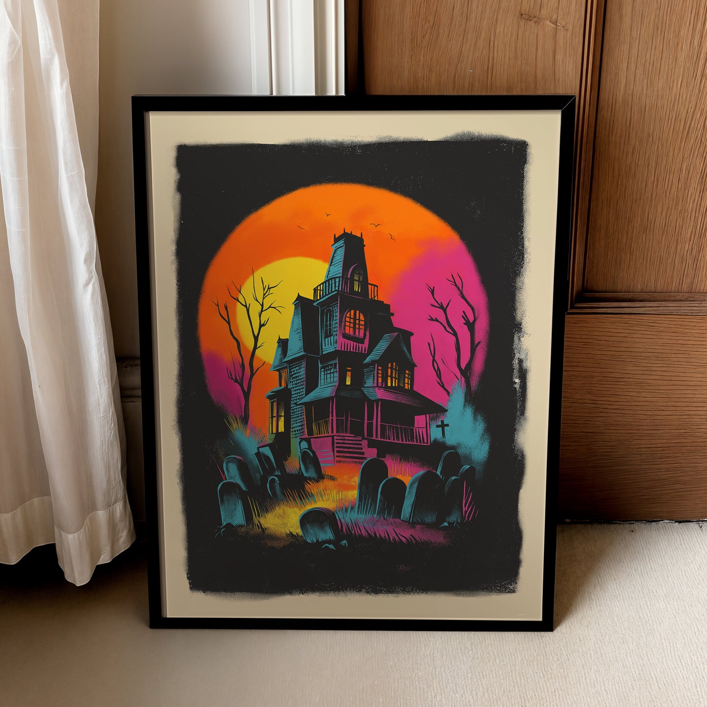 A framed art print featuring a spooky haunted house illustration in a retro neon style, leaning against a wooden door next to a curtain.