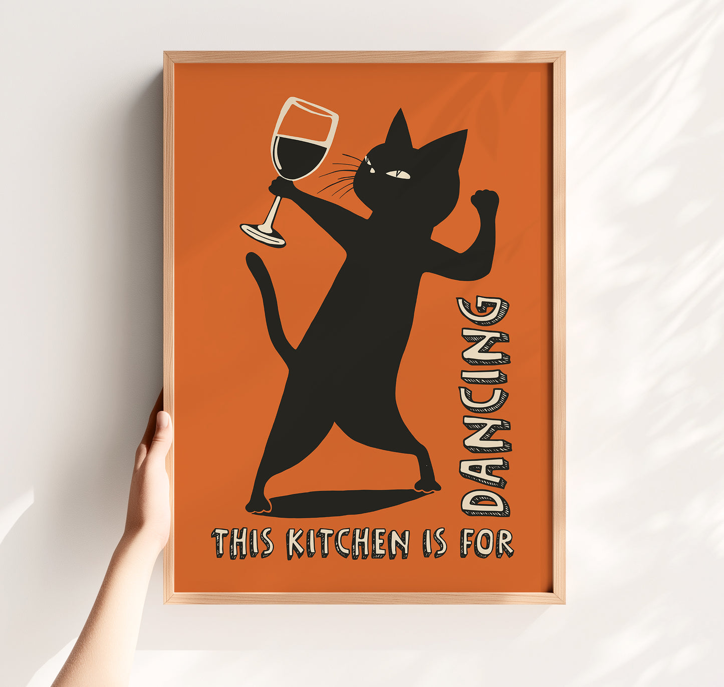 Retro illustration of a sassy black cat dancing while holding a wine glass on a burnt orange background, text reads "This Kitchen is for Dancing" in a vintage font.
