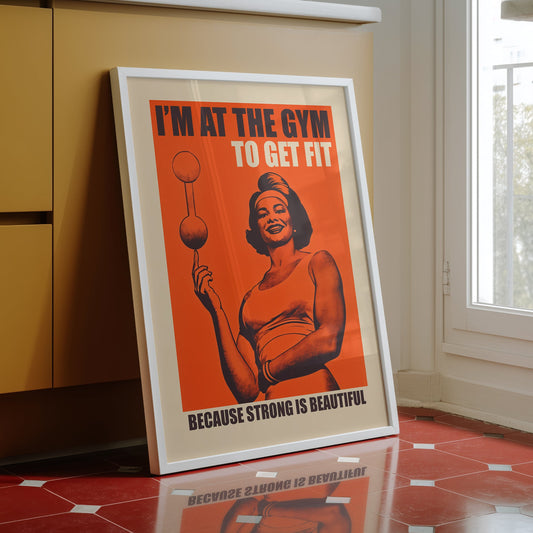 Vintage-style gym poster on an orange background featuring a muscular woman balancing a barbell on one finger with the text "I'M AT THE GYM TO GET FIT BECAUSE STRONG IS BEAUTIFUL."