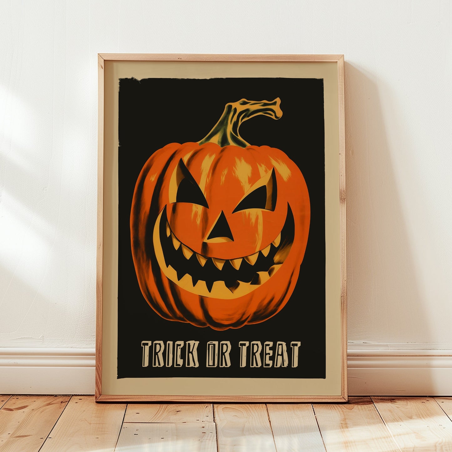 A framed Halloween art print featuring a carved orange jack-o'-lantern on a black background with the text 'TRICK OR TREAT' at the bottom, leaning against a white wall on a light wood floor.