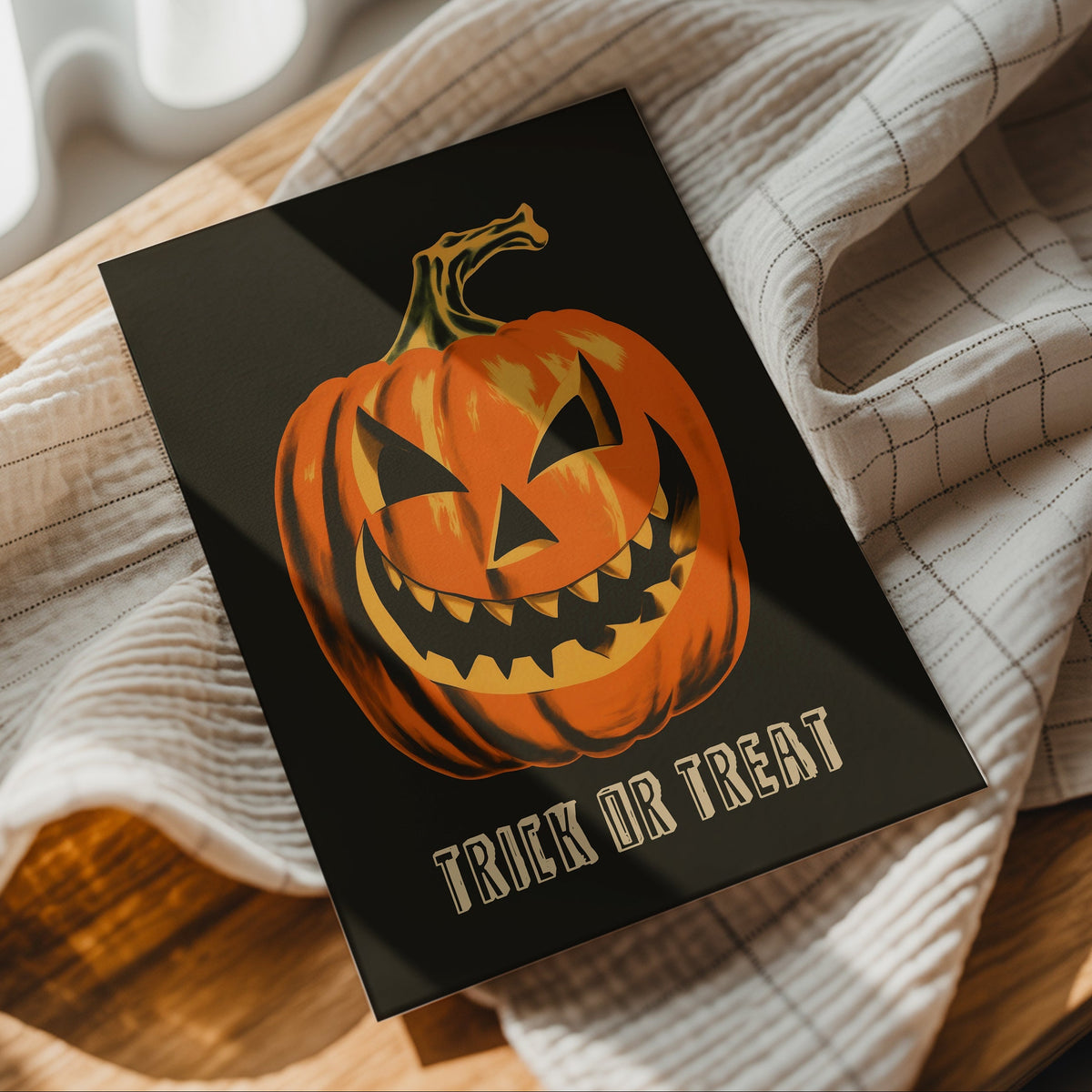 A Halloween greeting card featuring a carved orange pumpkin and the words 'TRICK OR TREAT' in gold, styled on a checkered beige cloth over a wooden surface.