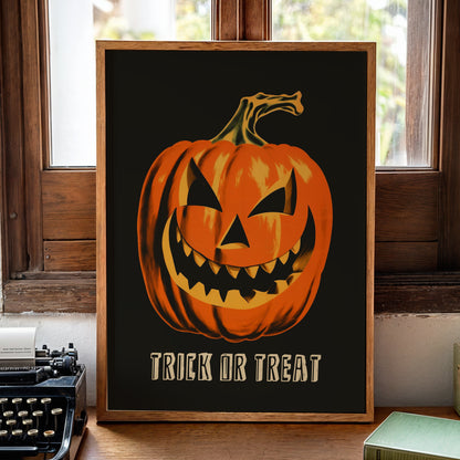 A framed Halloween art print featuring a carved orange jack-o'-lantern on a black background with the words 'TRICK OR TREAT' in cream. The print is displayed on a wooden desk in a vintage room setting next to a typewriter, books, and a candle.