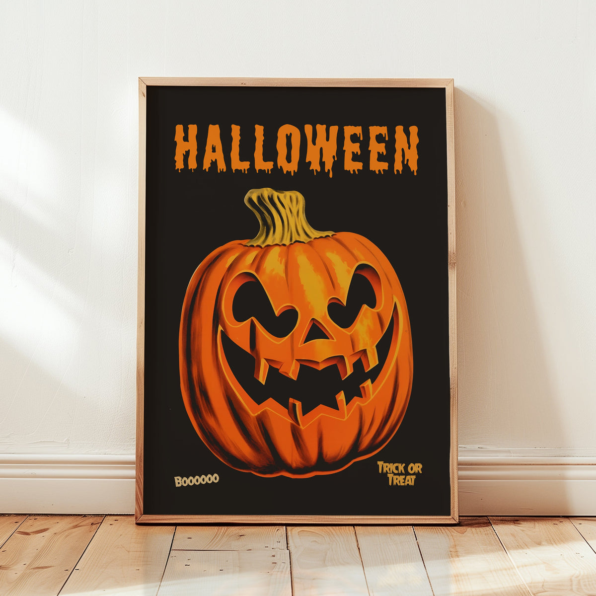 A framed Halloween art print featuring a carved orange pumpkin on a black background with the word 'HALLOWEEN' in dripping orange letters at the top, leaning against a white wall on a light wood floor.