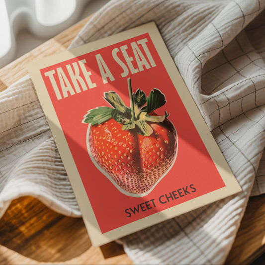 “Take a Seat Sweet Cheeks” strawberry bathroom poster styled on a beige checked blanket.