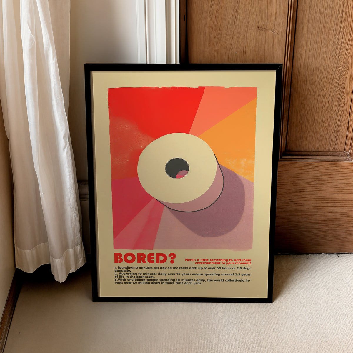 “Bored?” bathroom poster in a black frame leaning beside a curtain and wooden cabinet.