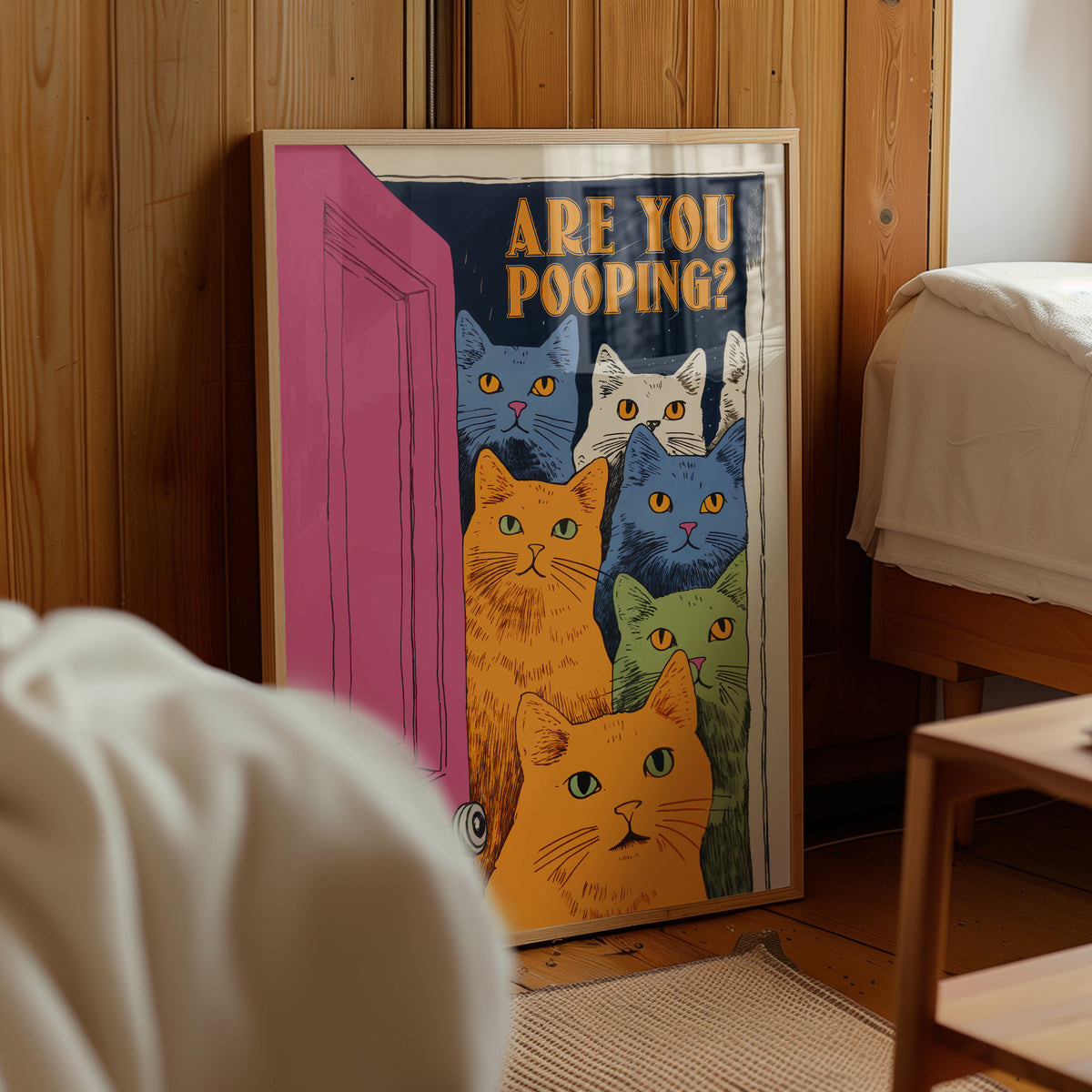 “Are You Pooping?” cat bathroom poster with six cats, framed beside a bed in a warm bedroom.
