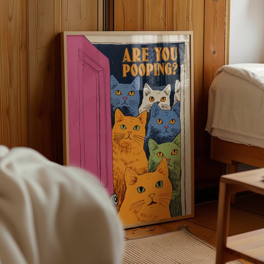 “Are You Pooping?” cat bathroom poster with six cats, framed beside a bed in a warm bedroom.
